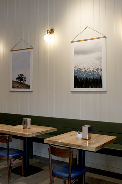 A close up of white paneling lining the walls and local art hanging behind wooden tables